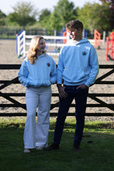 A man and a woman wearing matching oversized light blue Equestrian hoodies.