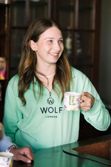 Women's Front View of Navy Embroidery Mint Green Quarter Zip whilst holding tea
